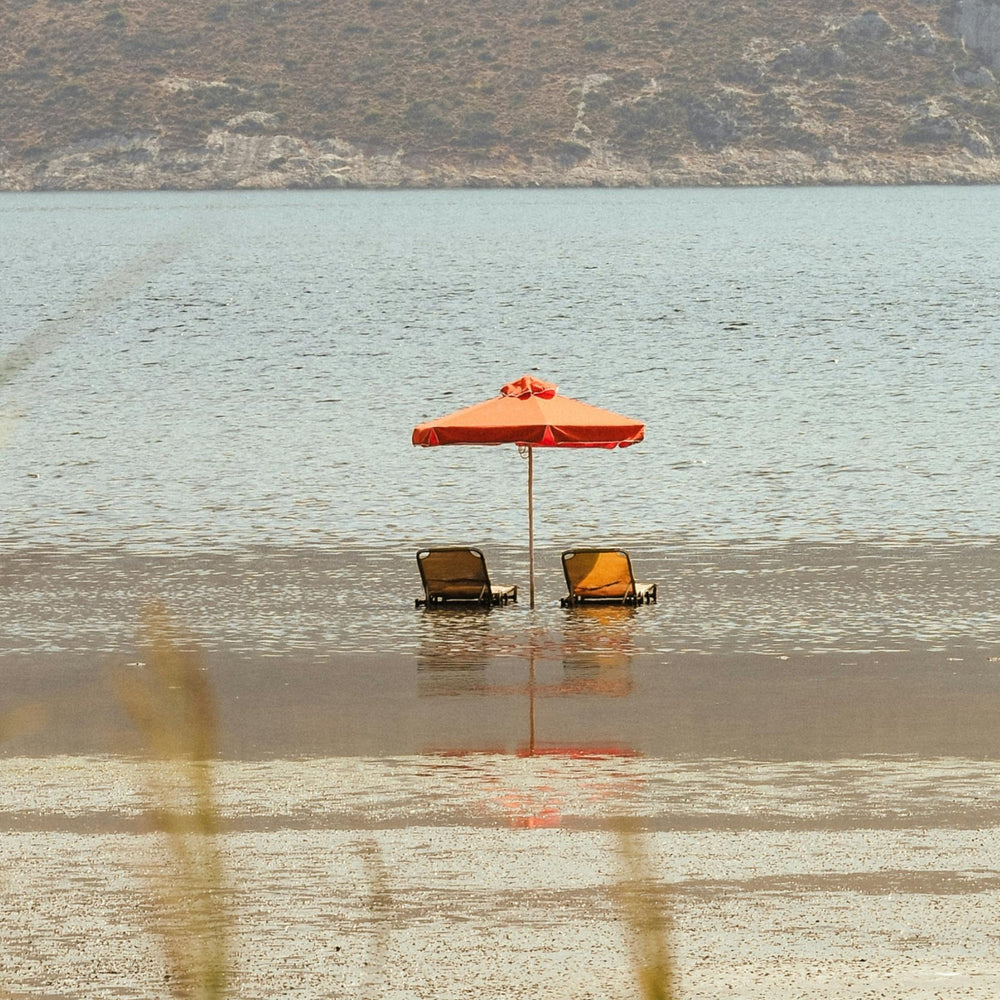 Contact Us page banner featuring a serene beach scene with two orange umbrellas and lounge chairs in shallow water, reflecting the calm and inviting atmosphere of Faeves.