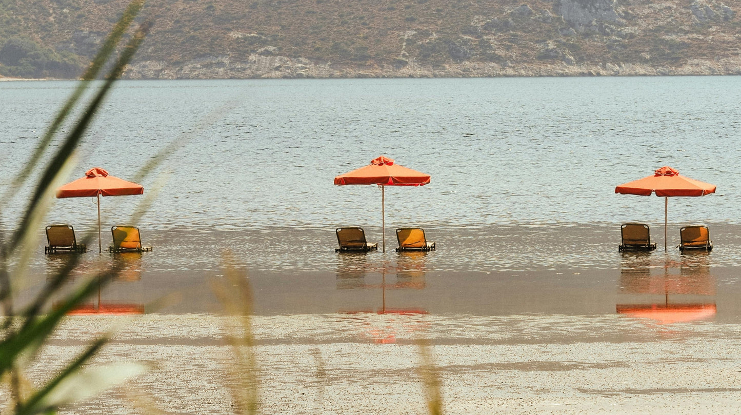 Contact Us page banner featuring a serene beach scene with two orange umbrellas and lounge chairs in shallow water, reflecting the calm and inviting atmosphere of Faeves.