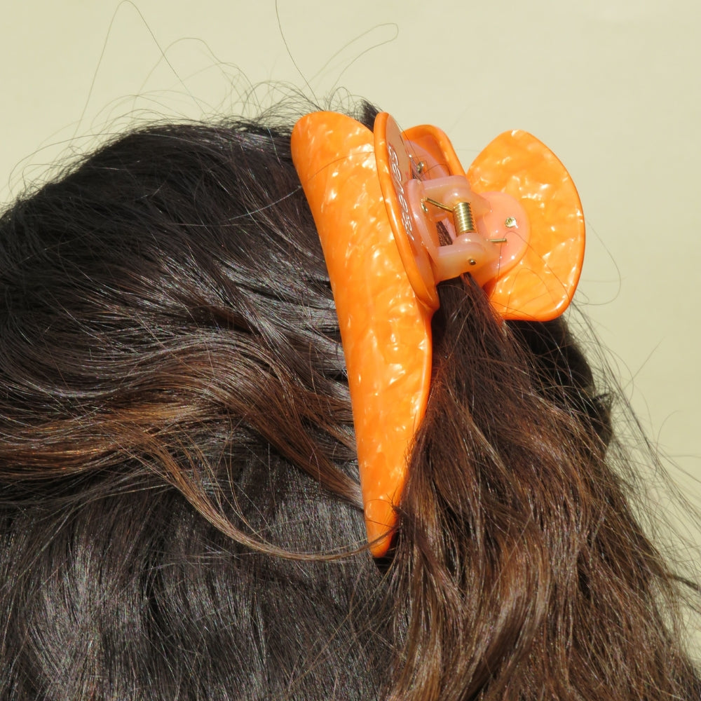 Close-up of an orange claw clip from Faeves, showcasing its vibrant color and sleek, glossy finish. The clip is detailed with strong, interlocking teeth that securely hold hair in place, highlighting its functional design and stylish appearance.