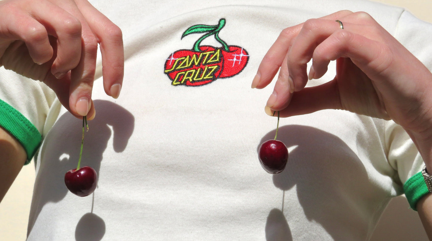 Shop All Products page banner featuring a close-up of a person holding cherries, with a Santa Cruz logo on their shirt, capturing the playful and vibrant essence of Faeves.